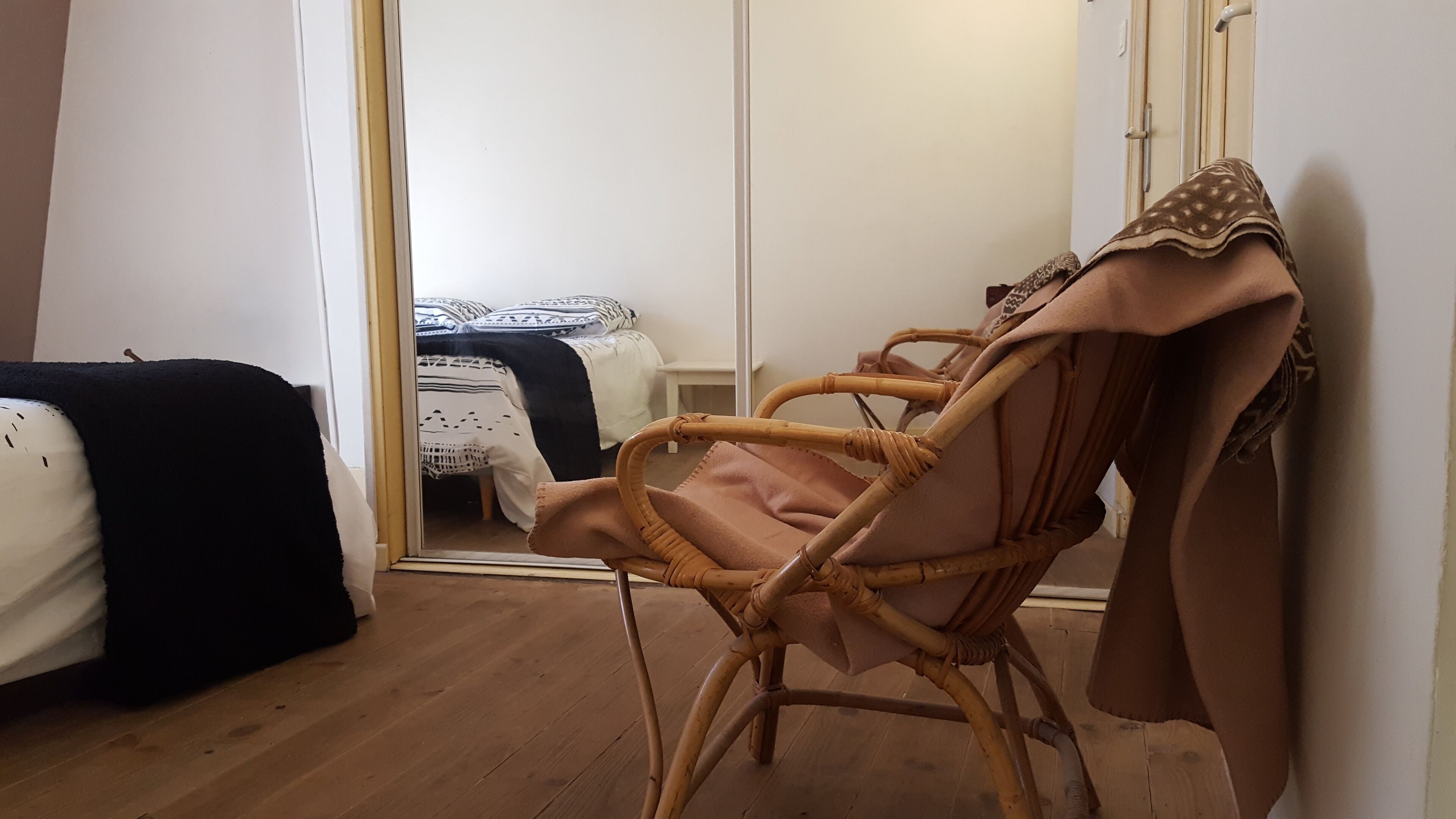 Una habitación con una silla de mimbre, una cama con colcha estampada y una puerta blanca.