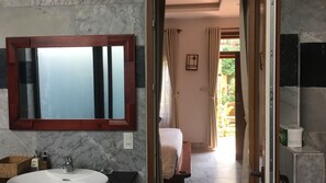 A bathroom with a marble sink, a wooden-framed mirror, and a view of a garden through an open door.