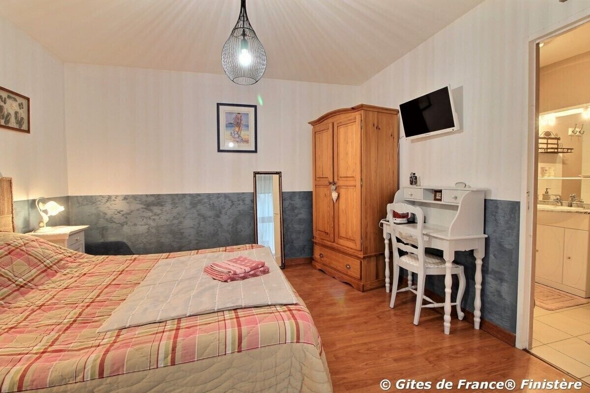 A bedroom with a bed, a desk, a chair, a wardrobe, and a television.