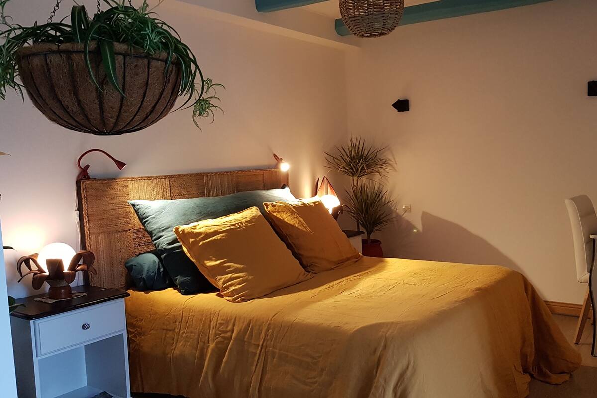 A bedroom with a bed, bedside tables, a hanging plant, and a desk with a chair.