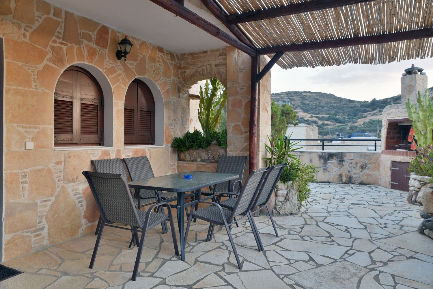 Une terrasse en pierre avec une table et des chaises, des fenêtres en arc de cercle et une vue sur la mer.