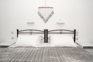 A neatly made bed with a grey striped bedspread, two white pillows, and a wooden headboard. There are bedside tables on either side of the bed, each with a white lamp. A decorative hanging ornament is visible above the bed.