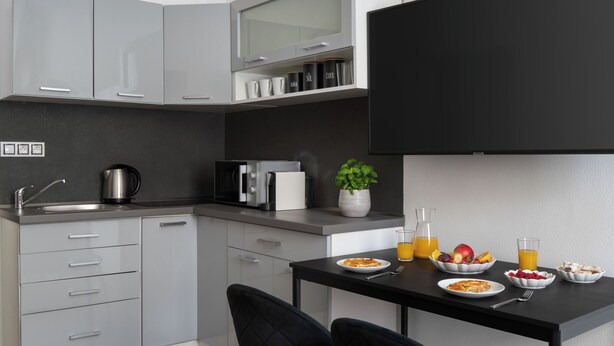 A modern kitchen with grey cabinets, a black countertop, and a dining area with a table set for breakfast. - Apartment Pekarska 29 by goodnite cz (Brno)