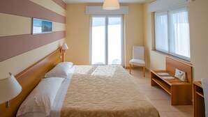 A hotel room with a bed, bedside lamps, a chair, a desk, and a large window. - Alpi (Baveno)