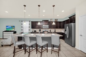 A modern kitchen with dark wood cabinets, a stainless steel refrigerator, a built-in microwave, and a central island with bar stools.