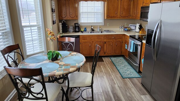 A kitchen with wooden cabinets, a stainless steel refrigerator, a dining table with chairs, and a window with blinds. - Great Home; Close to Everywhere. (Oak Grove)