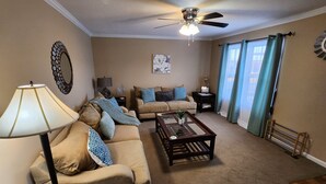 A living room with a beige sofa, a coffee table, a floor lamp, a ceiling fan, and a window with curtains. - Great Home; Close to Everywhere. (Oak Grove)