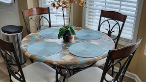 A round dining table with a patterned tablecloth, four chairs, and a potted orchid plant. - Great Home; Close to Everywhere. (Oak Grove)