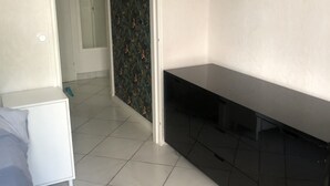 A room with a bed, a white nightstand, a black TV stand, and a door leading to another room.