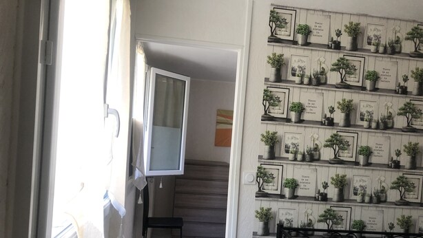A hallway with a staircase leading to a bedroom. The hallway features a wall with framed pictures and potted plants.