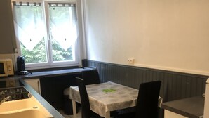 A compact kitchen with a dining area, a window with curtains, and a microwave on the counter.