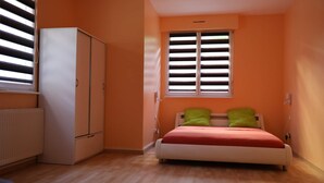 A bedroom with a bed, a wardrobe, a radiator, and a window with blinds. - Apartment near Basel / Mulhouse Airport (Saint-Louis)