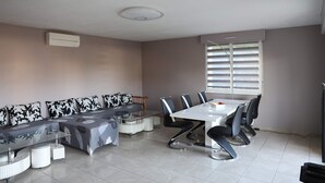 A modern meeting room with a long table, six chairs, a sofa with patterned cushions, and a window with blinds. - Apartment near Basel / Mulhouse Airport (Saint-Louis)