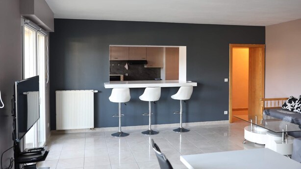 A modern kitchen with a built-in island and bar stools, a white radiator, and a large window. - Apartment near Basel / Mulhouse Airport (Saint-Louis)