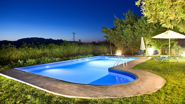 Una piscina con solárium de baldosas, rodeada de césped y árboles, con vistas a montañas al fondo.