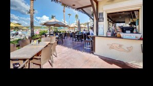 Een terras met tafels en stoelen, parasols en een bar, met een 'Welcome'-bord.