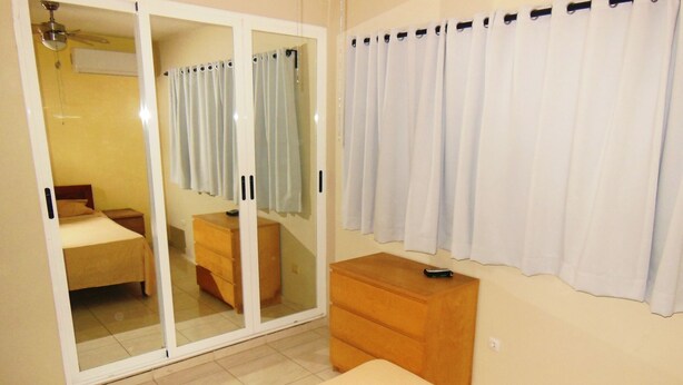 A bedroom with a bed, a wooden dresser, a sliding glass door, and a white curtain. - fresh apartment 90 m2,  with huge balcony (Bávaro)