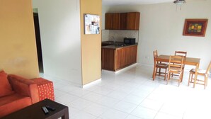 A living room with a sofa, a coffee table, and a dining area with a table and chairs. There is a kitchen area with wooden cabinets and a microwave. - fresh apartment 90 m2,  with huge balcony (Bávaro)