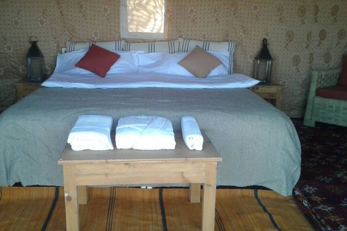 Una cama bien hecha con almohadas, una mesita de madera con toallas y una ventana con cortinas.