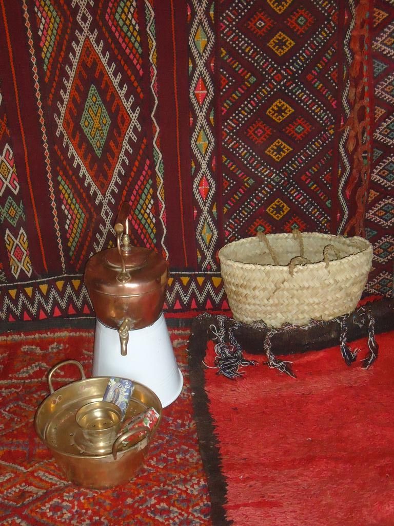 Decoración tradicional con un hervidor de cobre, una cesta tejida y un cuenco de metal sobre una alfombra roja.