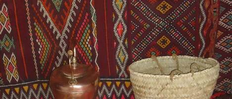 Decoración tradicional con un hervidor de cobre, una cesta tejida y un cuenco de metal sobre una alfombra roja.