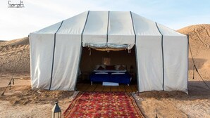 Une tente de désert avec un lit à l’intérieur, une moquette rouge et une lanterne posée sur le sol.