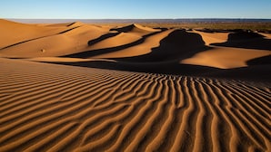 Un paysage désertique avec des dunes de sable ondulantes et un ciel bleu clair.