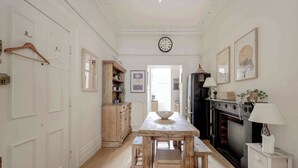 A kitchen with a wooden table, benches, a hanging wooden hanger, a clock, a fireplace, and a white cabinet.