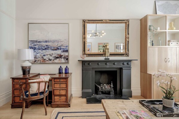 A living room with a fireplace, wooden furniture, a large mirror, and a painting on the wall.