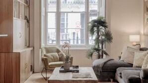 A living room with a large window, a sofa, a coffee table, and a bookshelf.