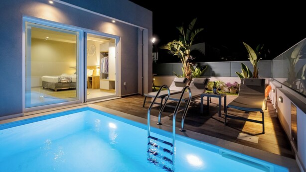 A modern outdoor pool area with a glass door leading to a bedroom, a lounge chair, and a small table with a fan. - Sarpidon Suites (Chania)