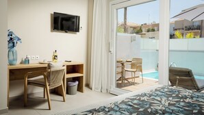 A hotel room with a bed, a desk, a chair, a TV, and a balcony with a pool. - Sarpidon Suites (Chania)