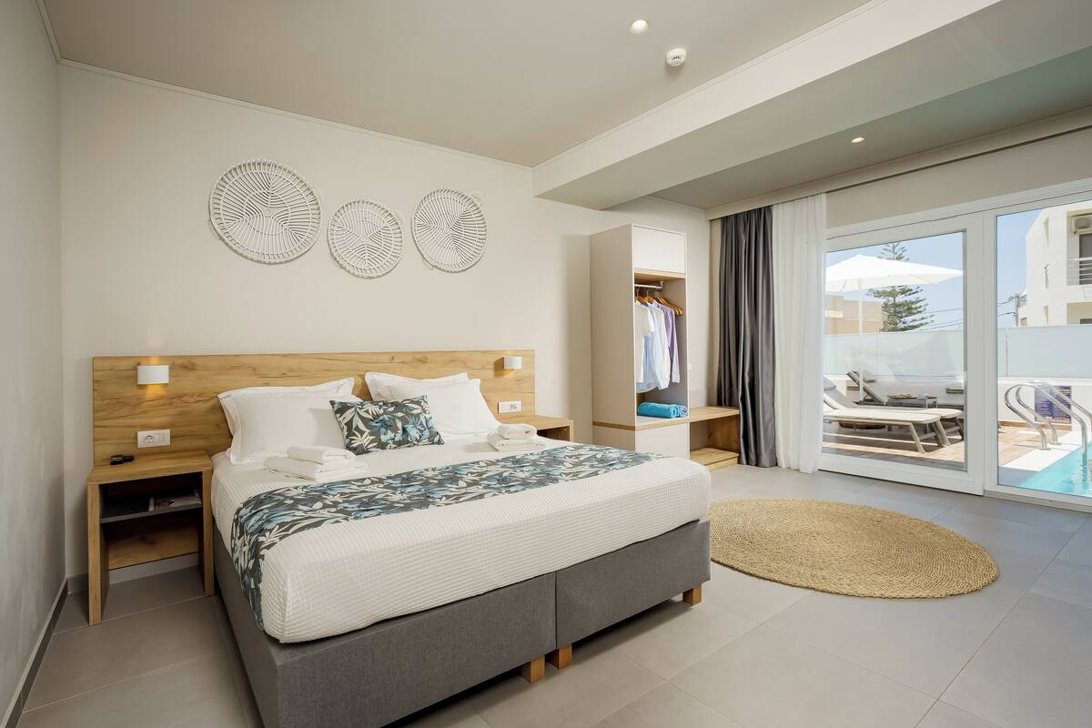Un dormitorio moderno con una cama grande, cabecera de madera, mesitas de noche y vistas a una piscina a través de un ventanal corredero.