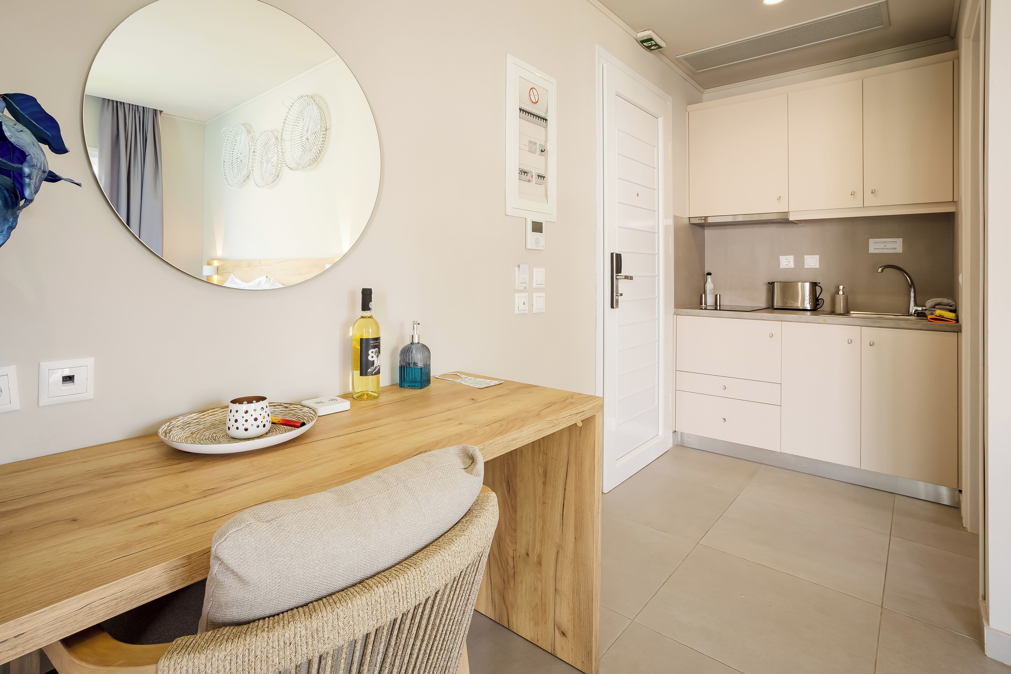 A modern kitchen with a wooden countertop, a round mirror, and a wicker chair.