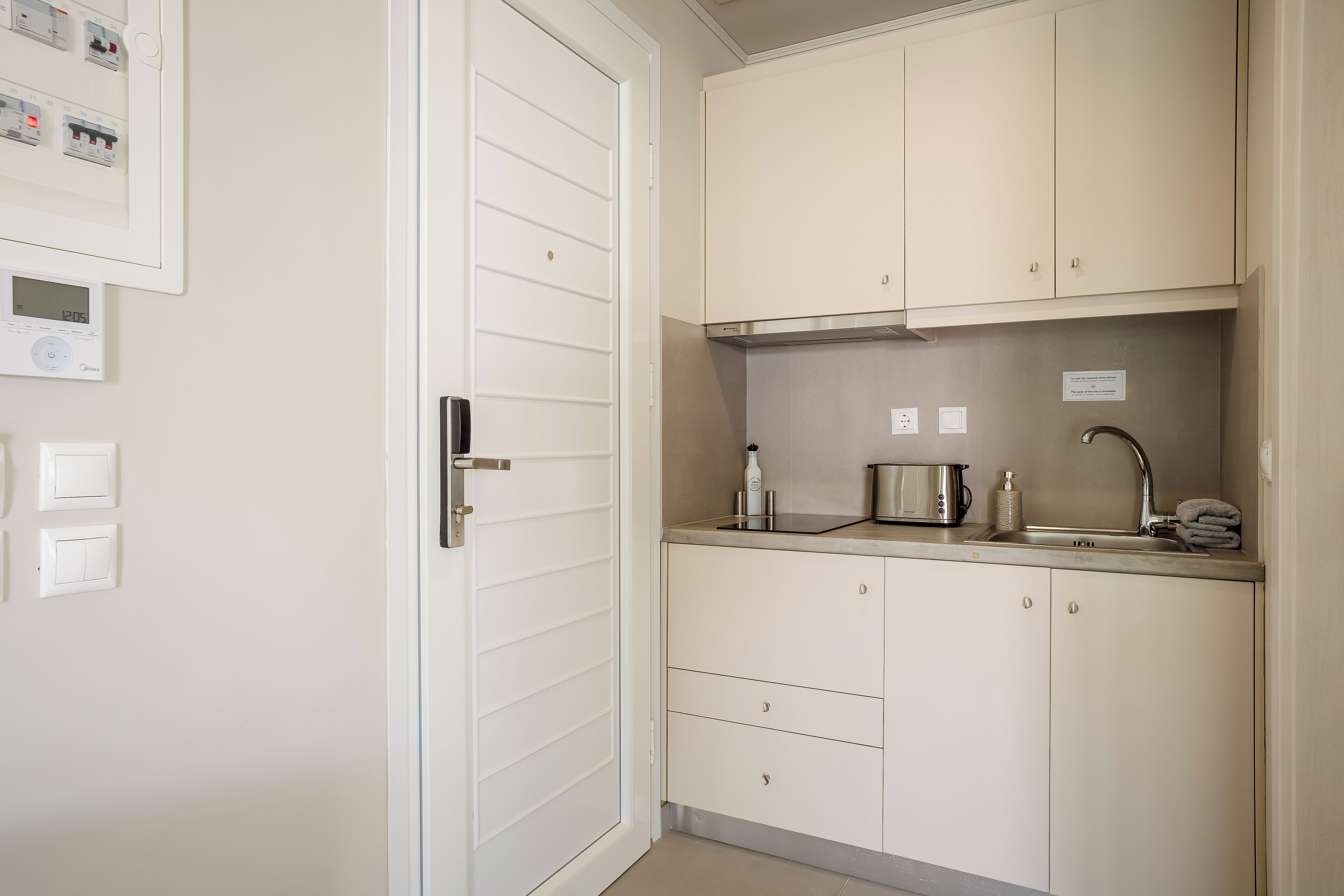 A kitchen with white cabinets, a stainless steel sink, and a toaster. There are three light switches on the wall.