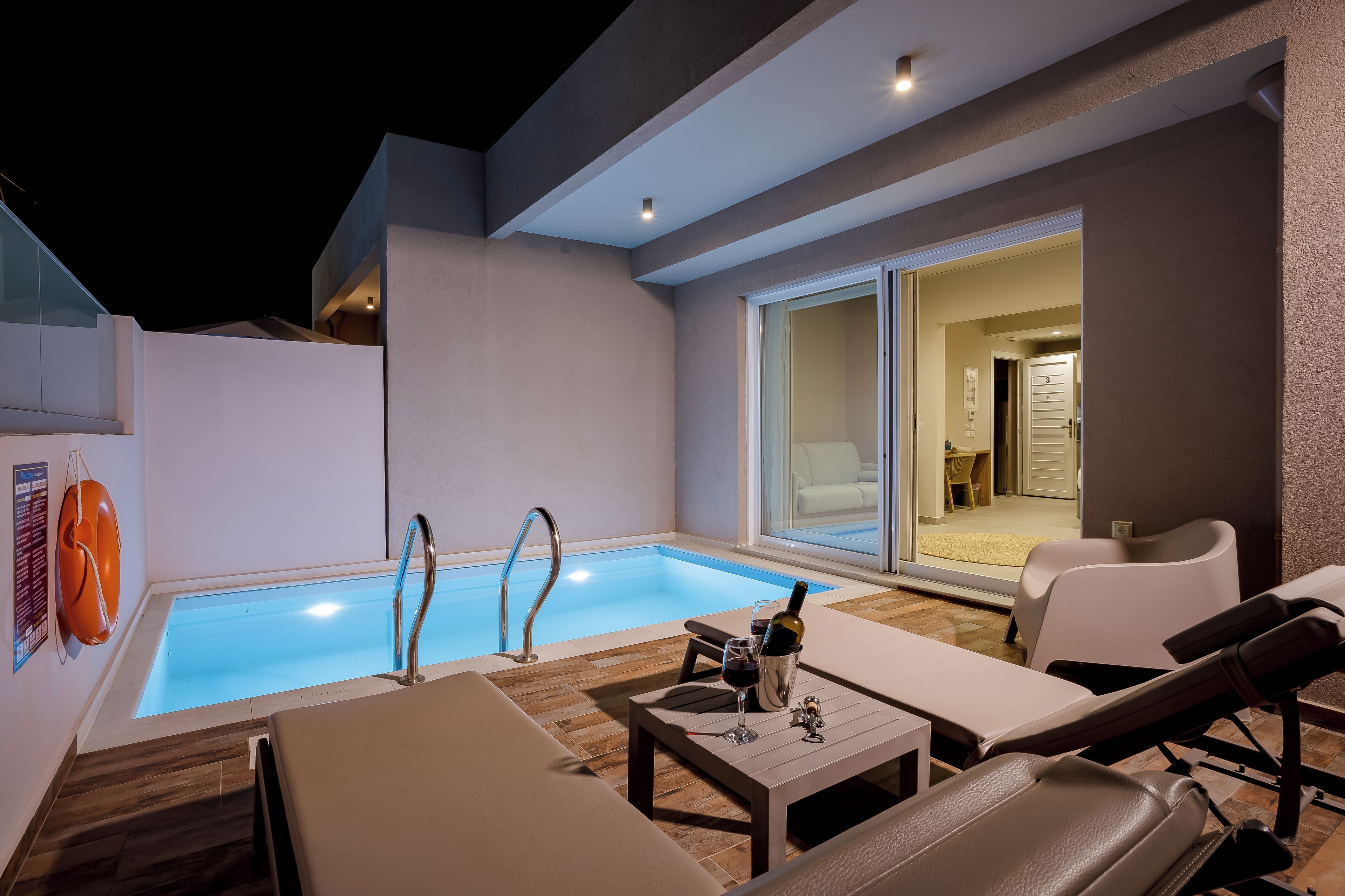 Ein moderner Poolbereich im Freien mit Liegestühlen, einem Tisch mit Flasche und Glas sowie einem kühlen, blauen Pool.