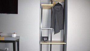A room with a black TV mounted on the wall, a small table with a decorative item, and a metal shelving unit with a jacket hanging on it. - Be Italian Room Bovio 23 (Naples)