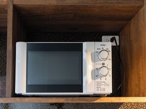 Un four à micro-ondes dans un tiroir en bois, doté de deux boutons de réglage et d’un câble d’alimentation.