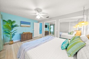 Ein Schlafzimmer mit Bett, Deckenventilator, Topfpflanze, Kommode und Spiegel.