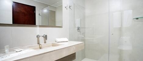 Un baño moderno con lavamanos de mármol, cabina de ducha con mampara de vidrio y panel de madera debajo del lavamanos.