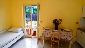 A compact room with a bed, a dining table with chairs, a vase of flowers, and a sliding glass door leading to an outdoor area. - Sole apartment with sea view and free wi fi (n ° 3) (Santa Domenica)