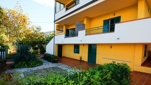 A two-story building with a yellow facade, a covered patio, and a garden area with various plants. - Sole apartment with sea view and free wi fi (n ° 3) (Santa Domenica)