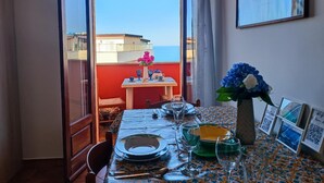 A dining area with a table set for four, a vase with flowers, and a balcony with a view of the sea. - Gaia Apartment with Sea View, 350m from the white beach of Tropea (TROPEA)