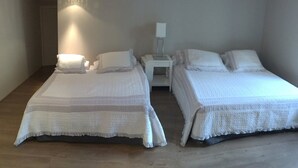 Ein Zimmer mit zwei Betten, jeweils mit weißer Bettwäsche und Kissen, einem Nachttisch mit Lampe und Holzboden.