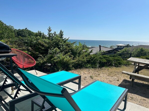 Un patio frente a la playa con dos sillones turquesa, una silla roja y una mesa de picnic.