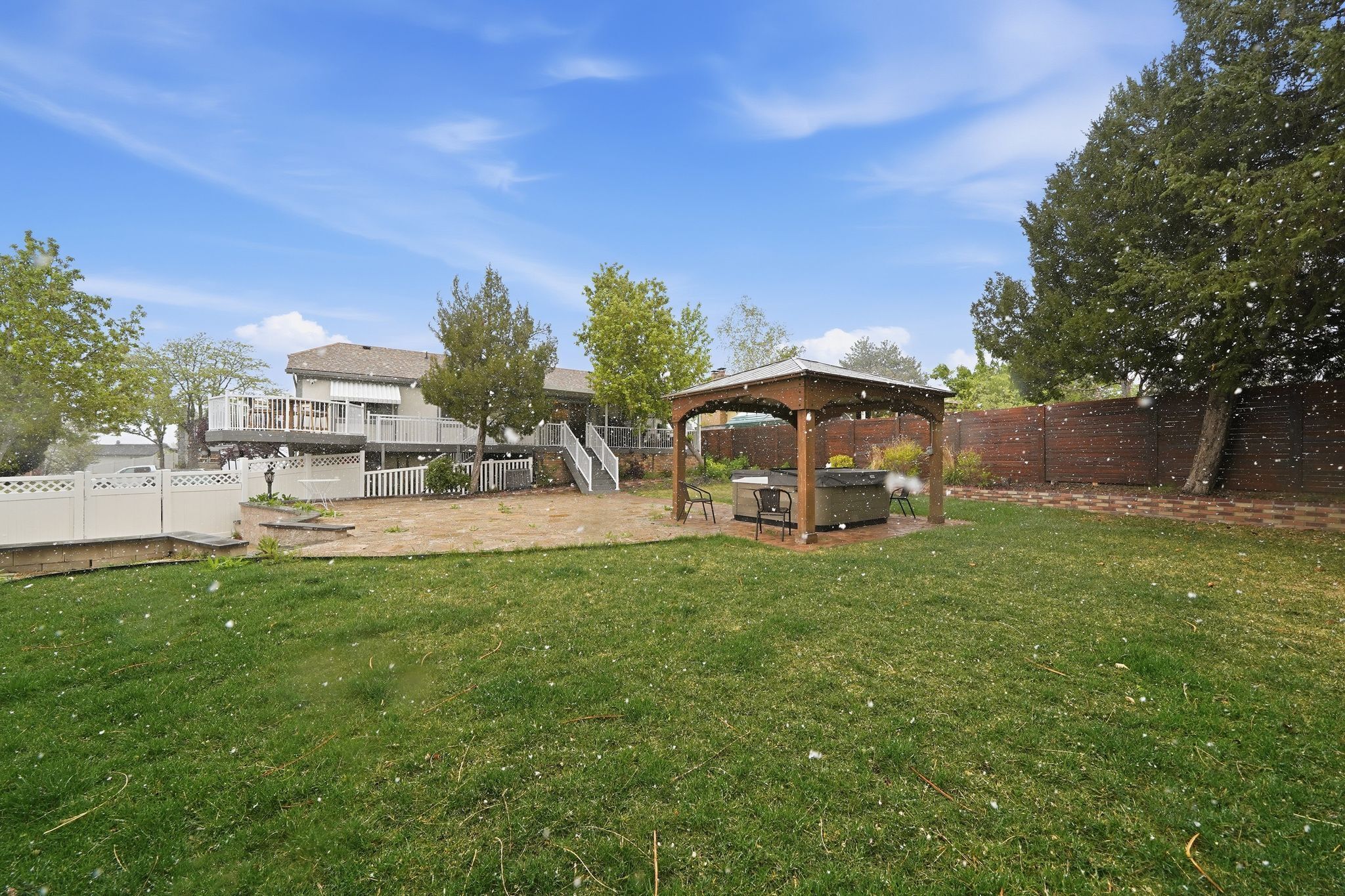 A backyard with a wooden gazebo, a white fence, and a house in the background.