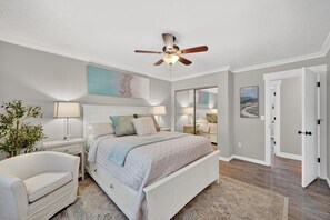 Une chambre à coucher avec un lit, des tables de chevet, une chaise, un ventilateur de plafond et une porte.