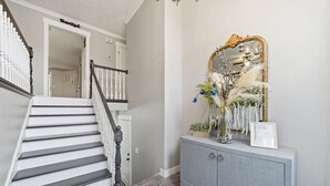 A staircase with a white railing, a grey console with a mirror, and a floral arrangement.