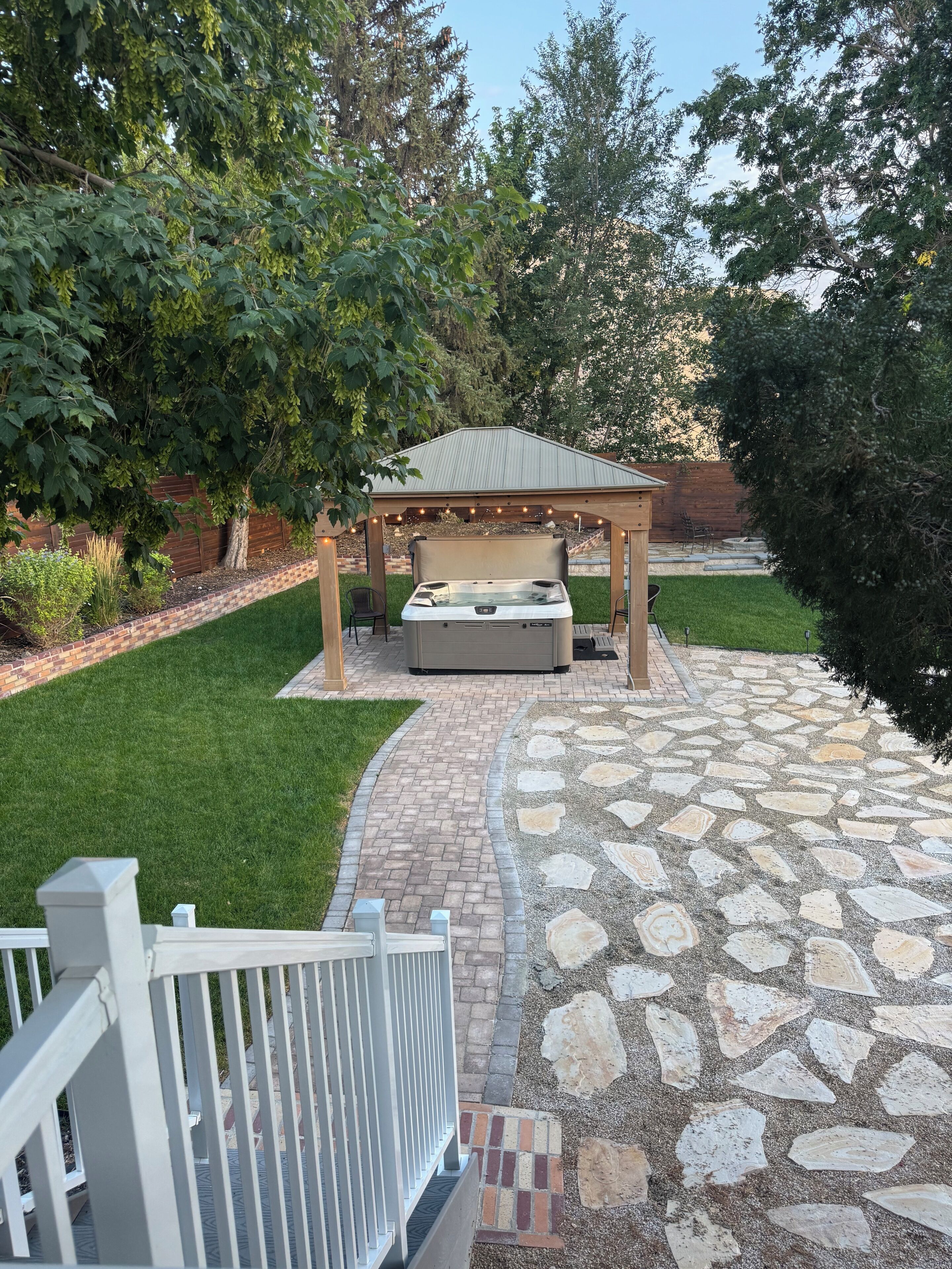 A patio with a hot tub, stone pathway, and a wooden pergola.