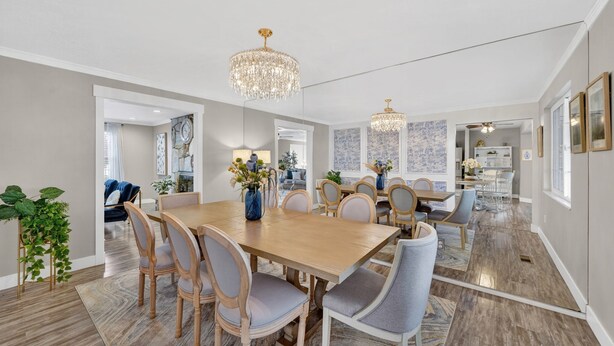 A spacious dining area with a wooden table and chairs, a chandelier, and a view into the kitchen.